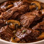 Bowl of beef tips and gravy cooked in a crockpot, served with rice.