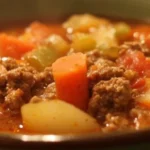 A bowl of hearty ground beef soup garnished with fresh herbs.