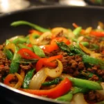 Ground beef stir fry with colorful vegetables in a skillet.