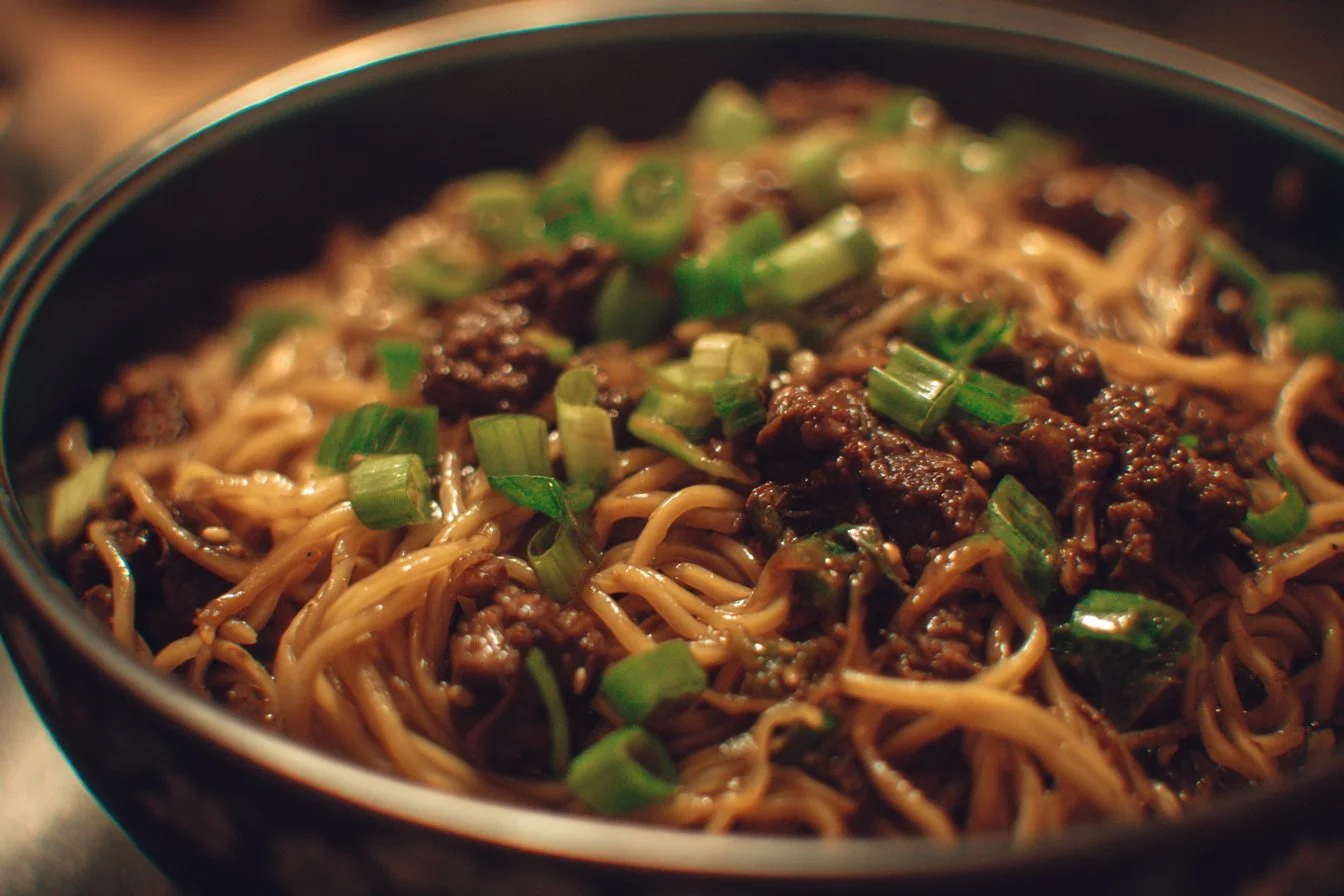 Bowl of Mongolian Ground Beef Noodles garnished with green onions and sesame seeds