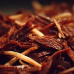 A plate of tender shredded beef garnished with herbs and spices.