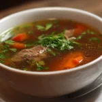 Bowl of savory beef broth soup garnished with fresh herbs and vegetables