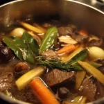 Homemade beef stock simmering in a pot with vegetables and spices.