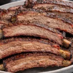 Delicious smoked beef ribs garnished with herbs on a wooden cutting board.