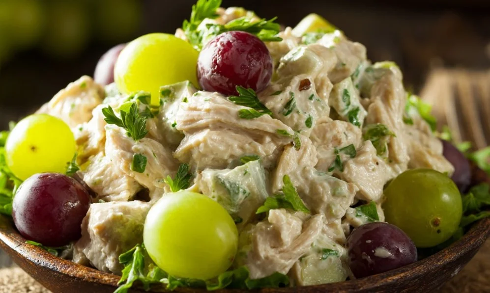 A bowl of chicken salad with grapes, celery, and walnuts served on a wooden table