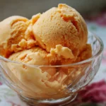 A bowl of creamy homemade peach ice cream with fresh peach slices on top