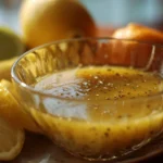 A bowl of fresh lemon vinaigrette dressing with lemon slices and herbs