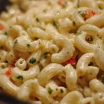 A bowl of creamy macaroni salad with vegetables and dressing served on a picnic table.