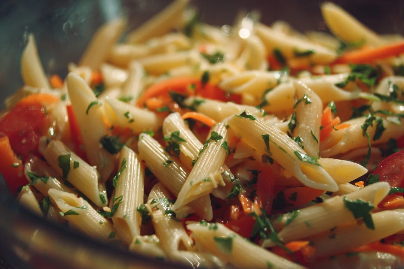 Colorful pasta salad with Italian dressing, veggies, and garnishes.