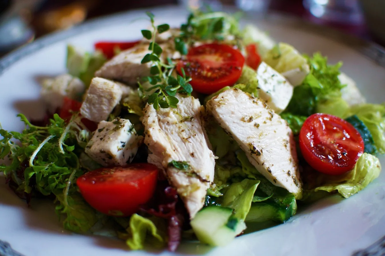 Healthy chicken salad served in a bowl with fresh vegetables and herbs.