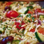 Colorful orzo salad with fresh vegetables and herbs in a serving bowl.
